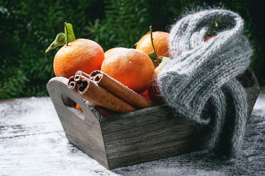12271263-Wooden-basket-with-tangerines-cinnamon-sticks-and-scarf-over-wooden-background-with-snow-and-cone
