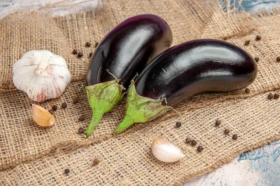 front-view-aubergines-garlic-black-pepper-straw-tablecloth_140725-108338